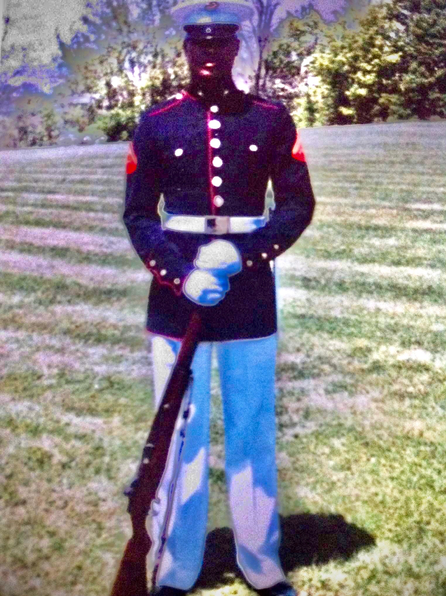 A Marine in dress blues standing at parade rest on a parade field