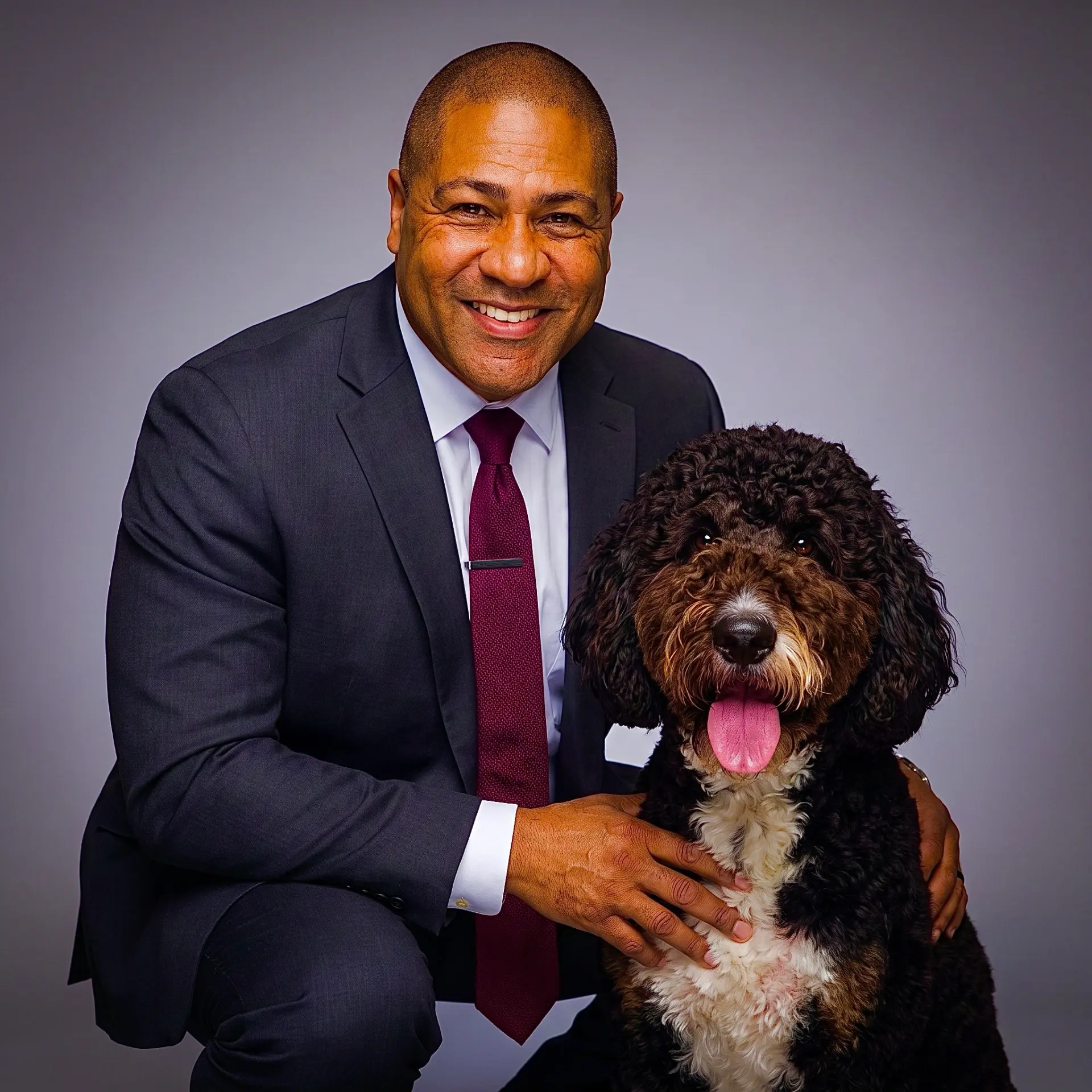 Kevin Lewis, founder of Mr. Finnster Unleashed, in a dark suit and burgundy tie with Finn, his rescued Bernedoodle